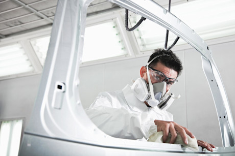 Man, 40s, wearing protective gear for painting auto parts. Working on vehicle rear door