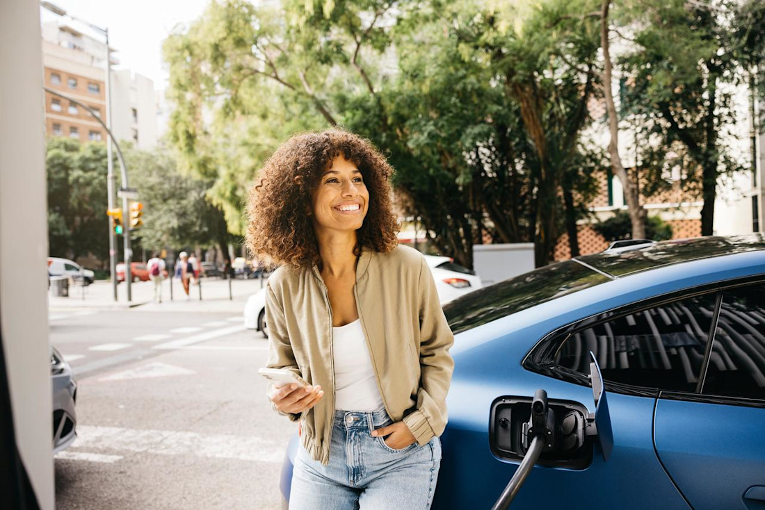 Woman leaning at charging blue electric car