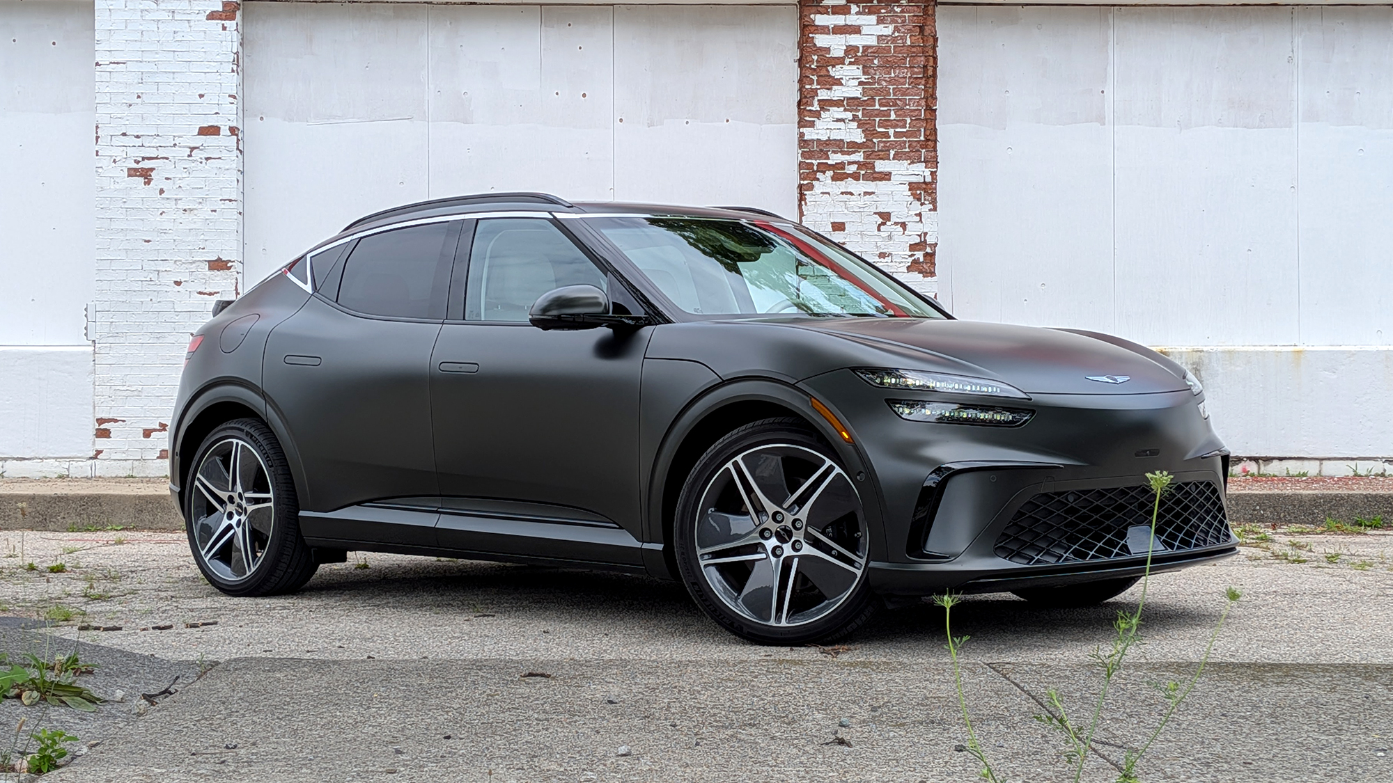 Dark grey 2026 Genesis GV60 parked in front of a white brick wall