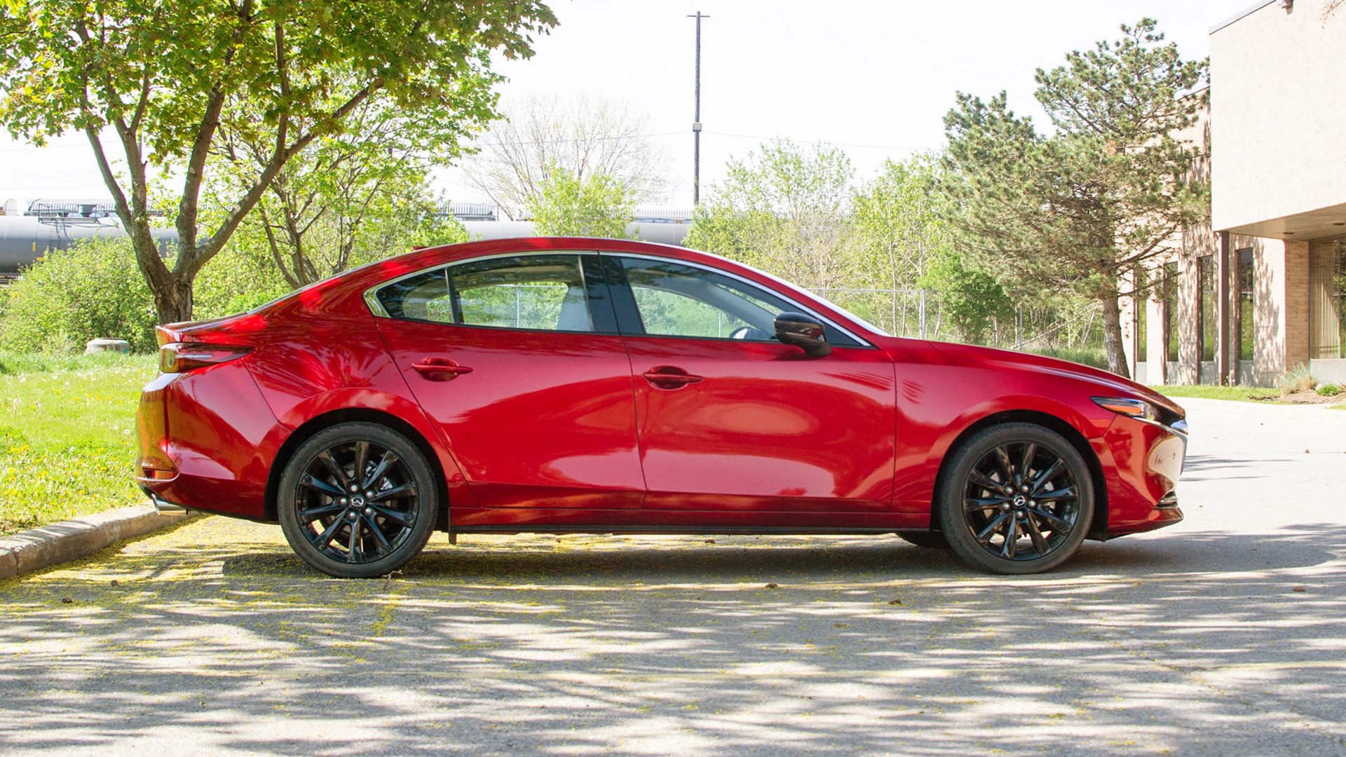 A side profile of a red Mazda 3 GT Turbo parked on the roadside.