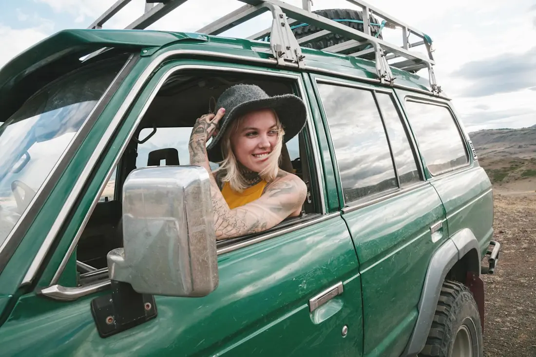 Blond woman with hat sitting in green car laughing Blond woman with hat sitting in green car laughing