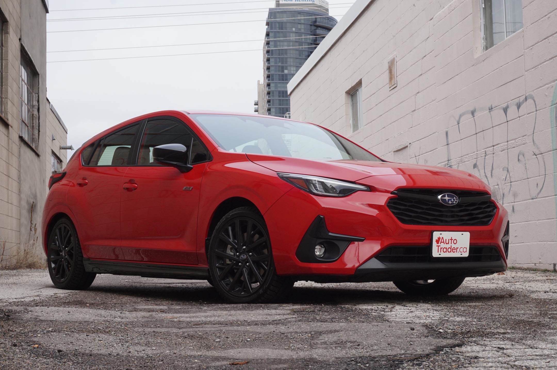 A red Subaru Impreza parked inbetween 2 buildings, showcasing its sleek design and vibrant color.