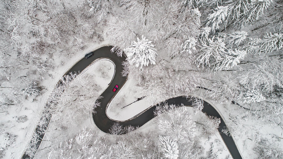 Winterreifenpflicht im Ausland: kurvige Straße im verschneiten Wald (Luftaufnahme)