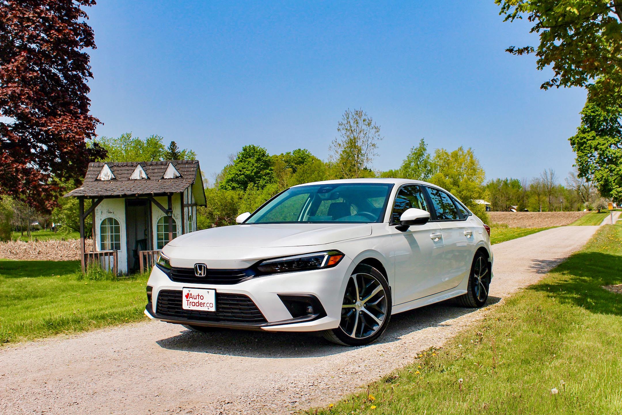 A white Honda Civic Sedan Touring rests on a country road, highlighting its modern features and stylish appearance