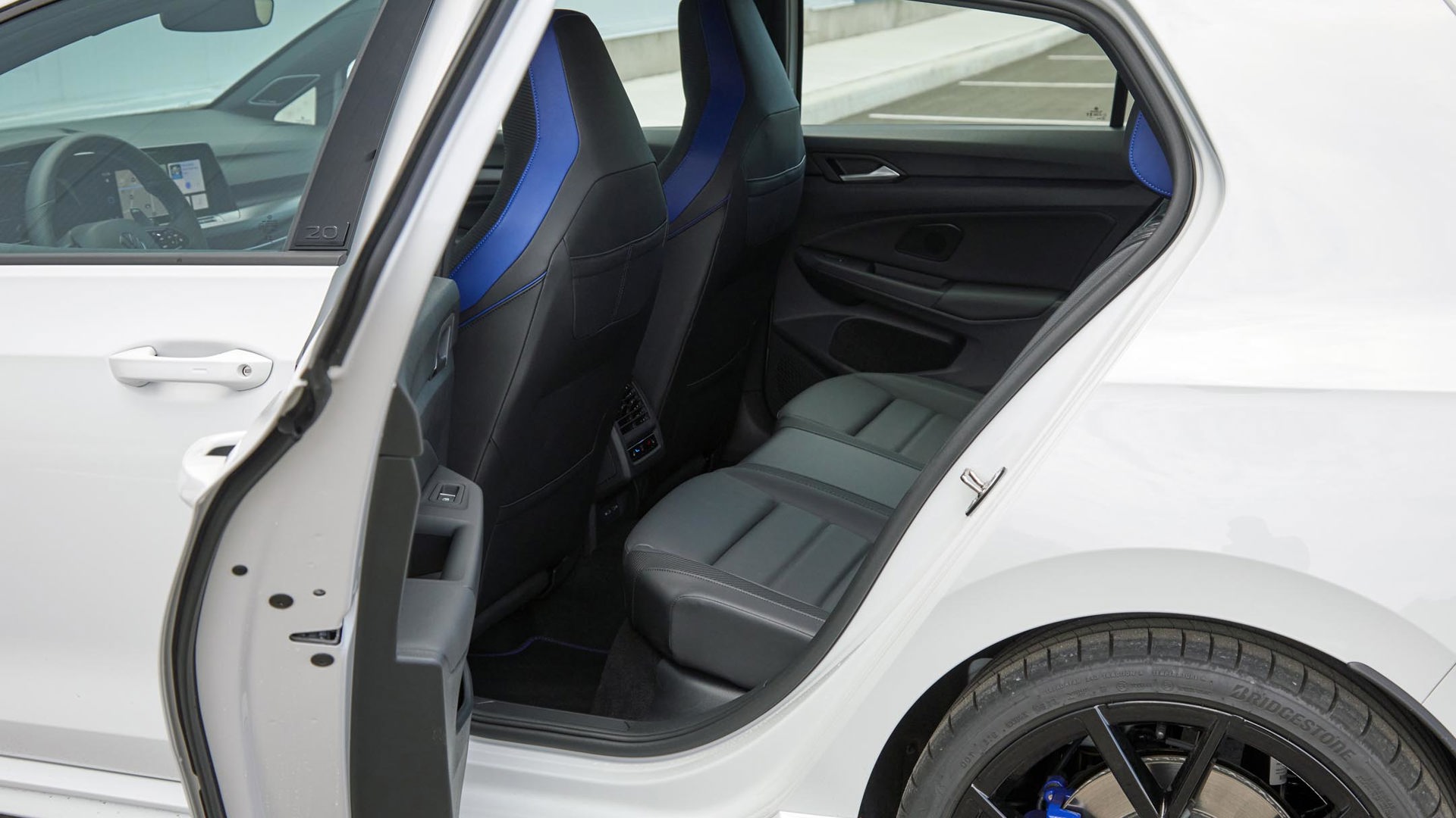 An open door of a white Volkswagen Golf R, revealing three passenger seats and their stylish blue and black interior seats.